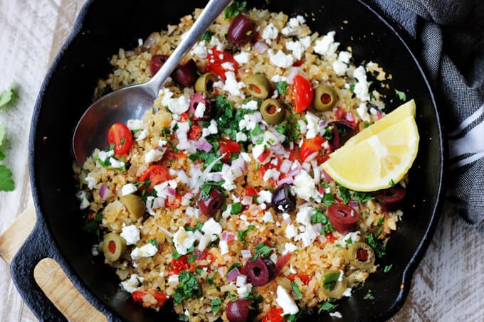 Fried riced cauliflower with Mediterranean twist in a skillet with spoon and lemon