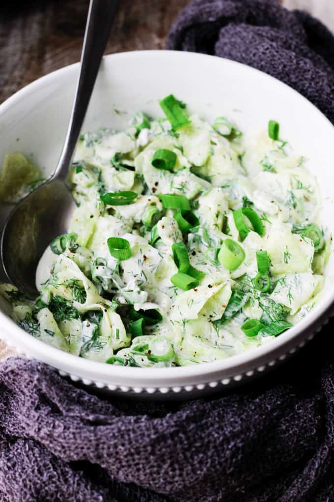 Polish cucumber salad - mizeria in a bowl with spoon in it and towel around it