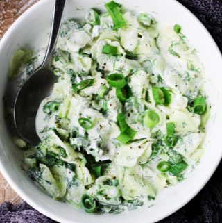 Polish cucumber salad in a white bowl with spoon; overhead shot, horizontal