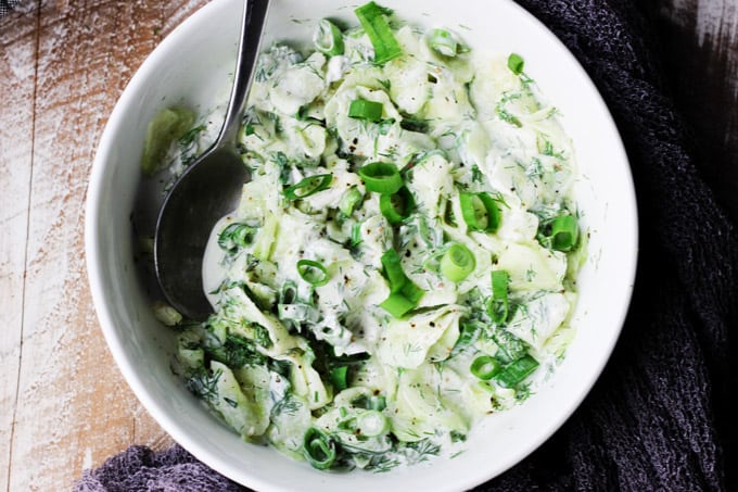 Polish cucumber salad in a white bowl with spoon; overhead shot, horizontal