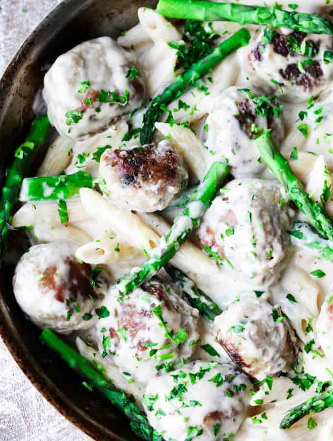 Turkey meatballs with asparagus in creamy alfredo sauce in a pan, overhead shot