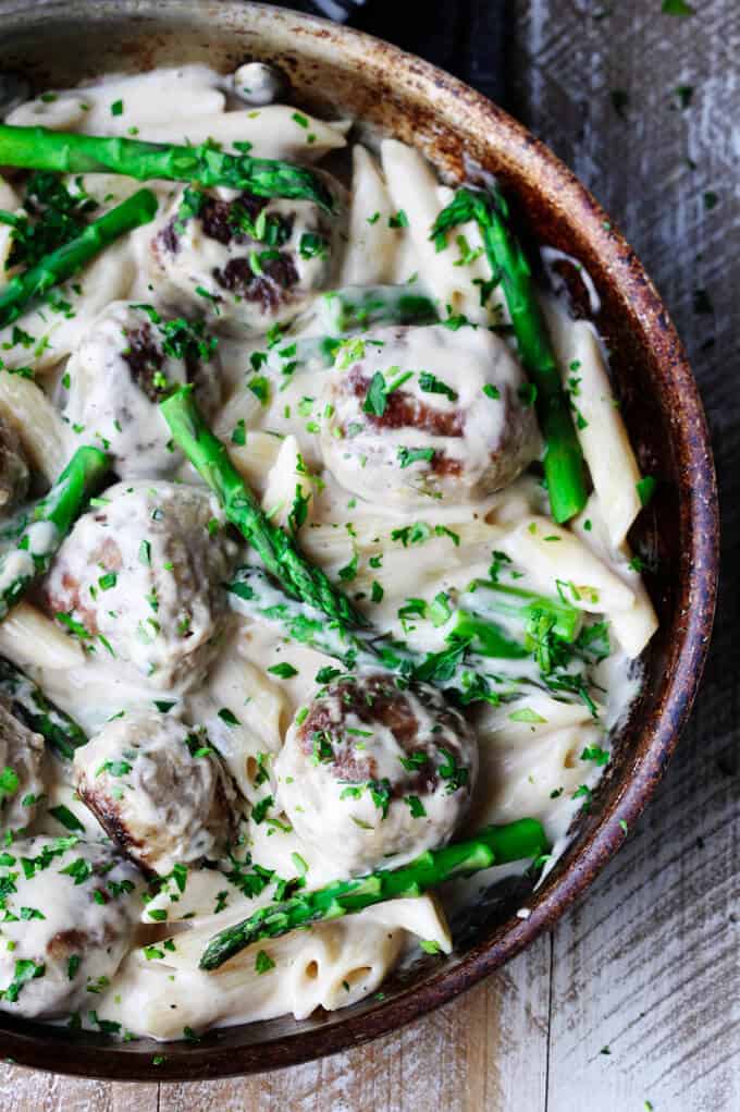 turkey meatballs and asparagus in creamy Alfredo sauce in a frying pan on a board