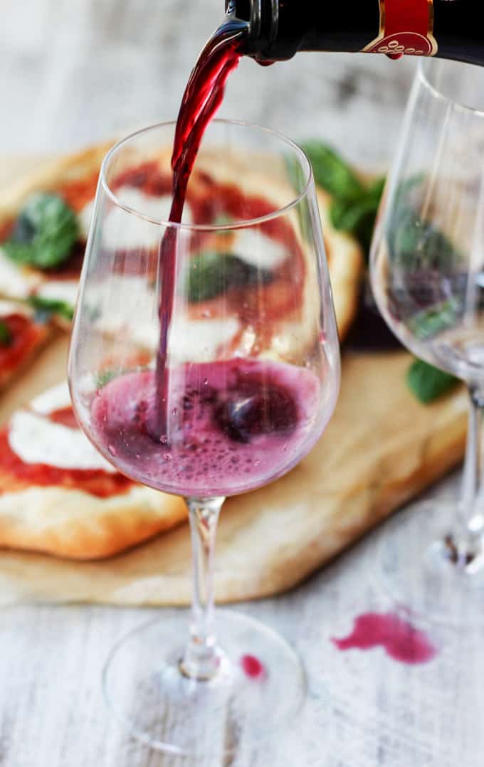 Pouring red wine into the glass with margherita pizza in a background