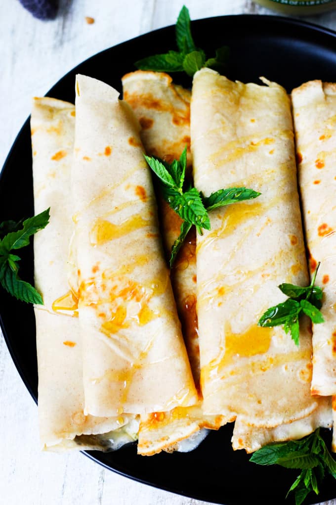Apple Sauce Crepes with Honey Ricotta rolled on a black plate
