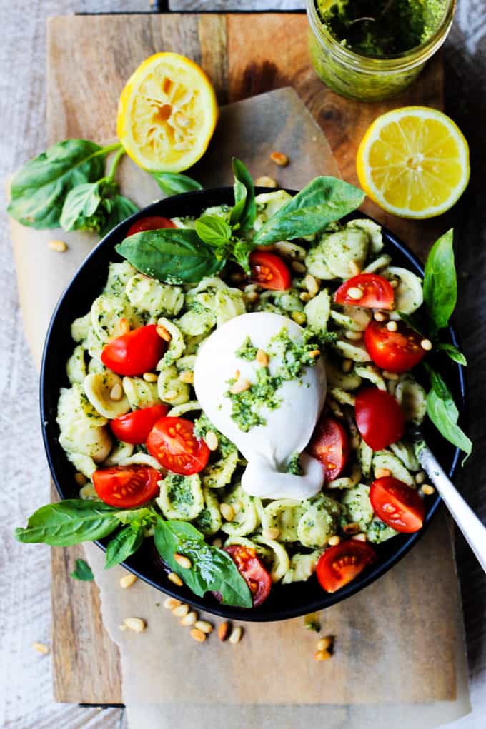 Black bowl of pesto pasta with tomatoes and Burrata cheese on top