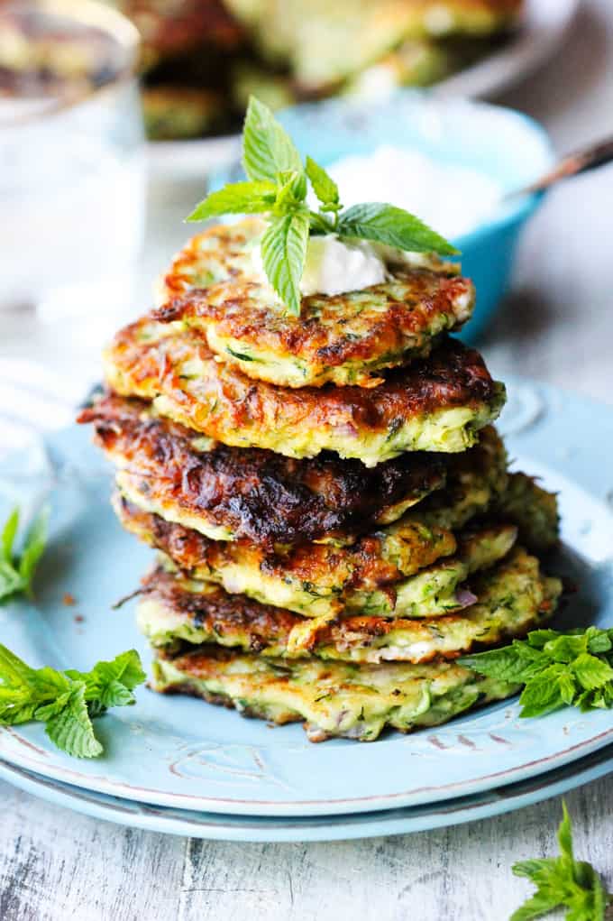 Greek Zucchini Fritters with Feta, called 'Kolokithokeftedes' stuck up on a blue plate with mint and dollop of yogurt.