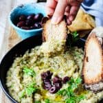 Melitzanosalata - Greek Eggplant Dip in a bowl with hand bread dipped in it