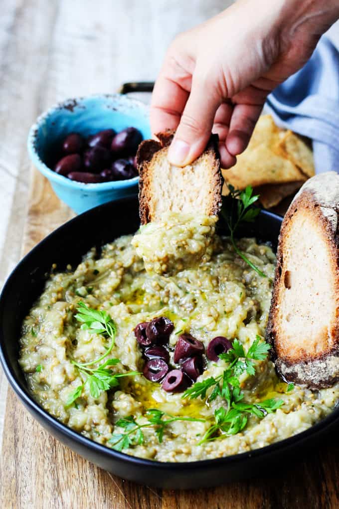 Melitzanosalata - Greek Eggplant Dip in a bowl with hand bread dipped in it