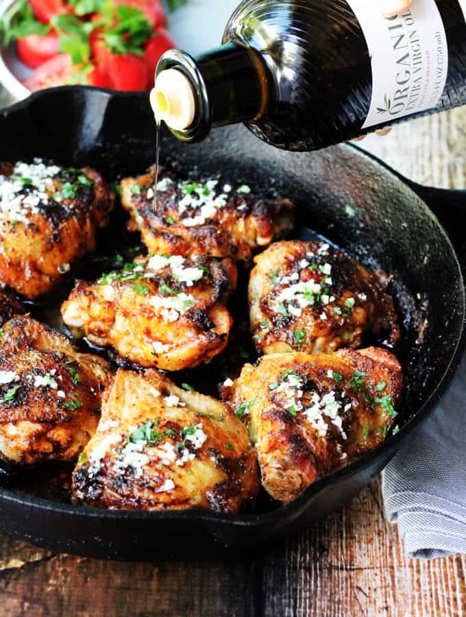 Olive Oil Chicken Mediterranean Style in a skillet with oil pouring over