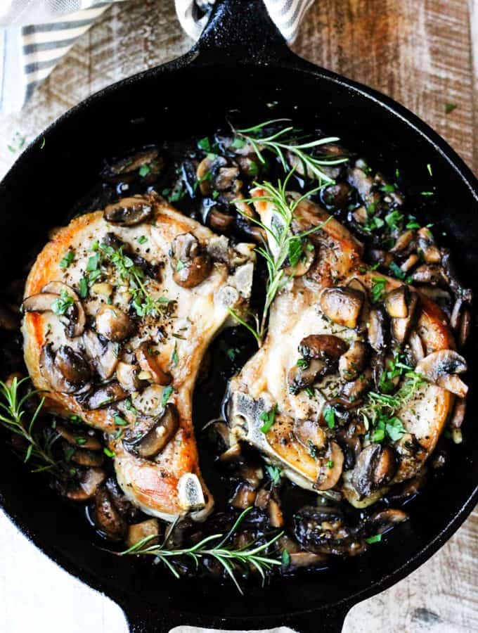 Mushroom pork chops with garlic butter and herbs in a skillet