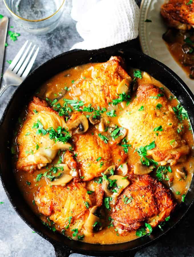 Chicken Chasseur in a skillet with fork on a side and water behind