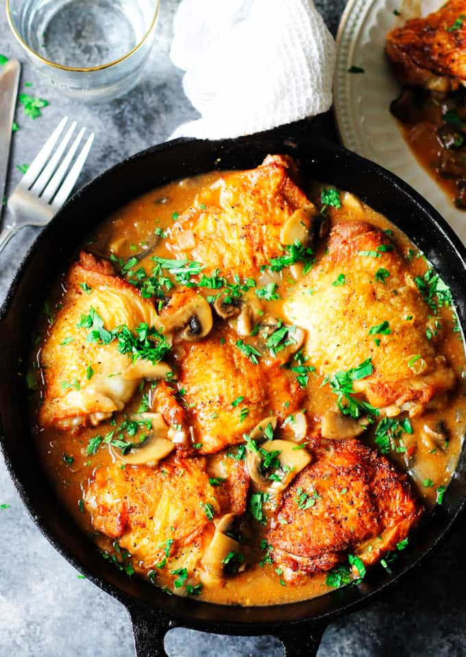 Chicken Chasseur in a skillet with fork on a side and water behind 