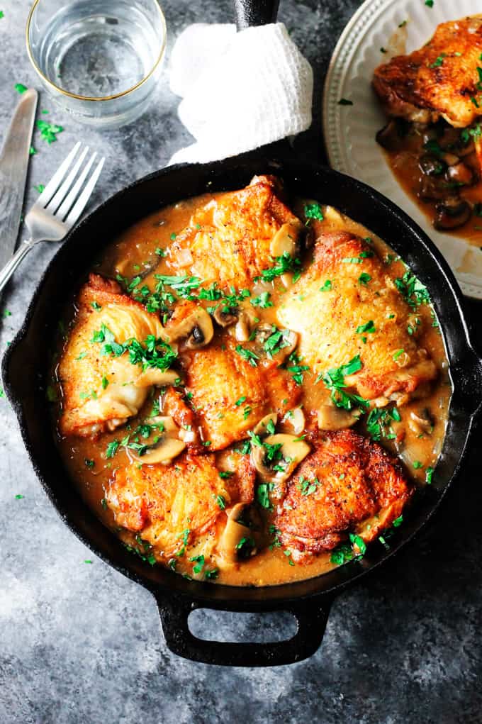 Overhead shot of French chicken chasseur in black skillet with water behind