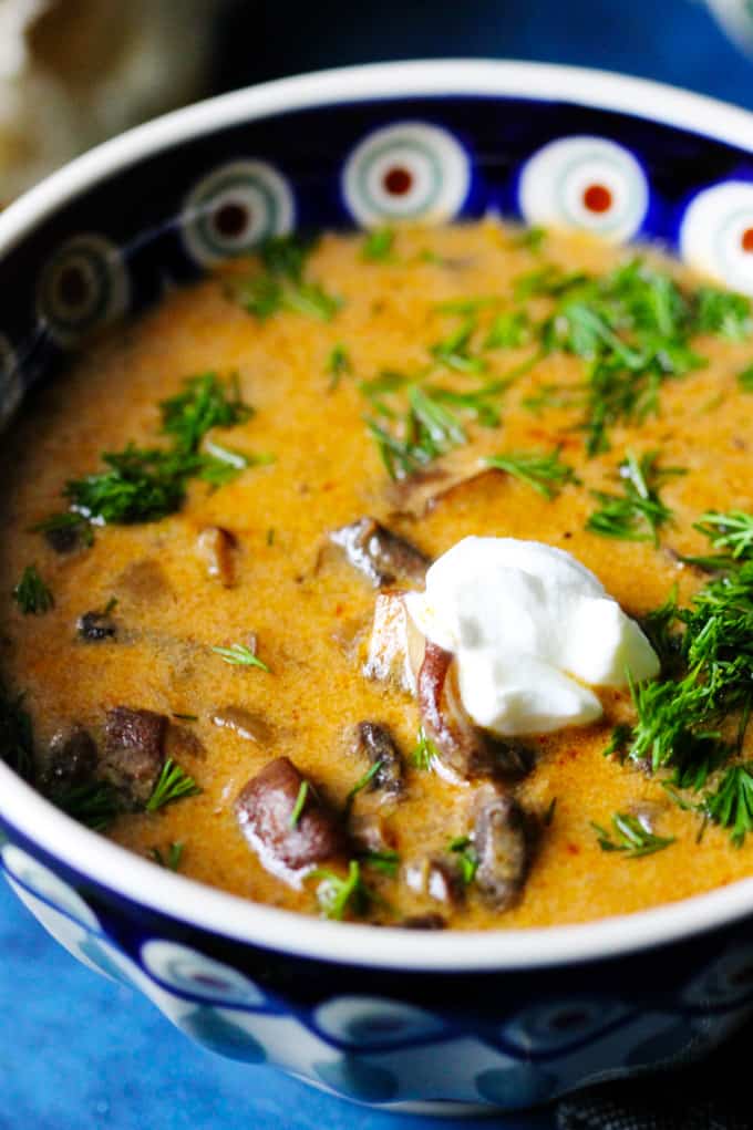 Hungarian mushroom soup in a blue bowl with dill and sour cream dollop