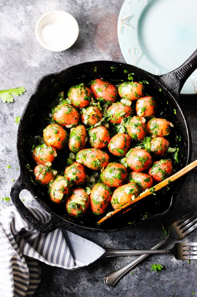 Parsley potatoes in a skillet with wooden spoon and plate on a side