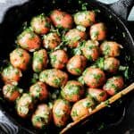 Overhead shot of parsley potatoes in a skillet with wooden spoon