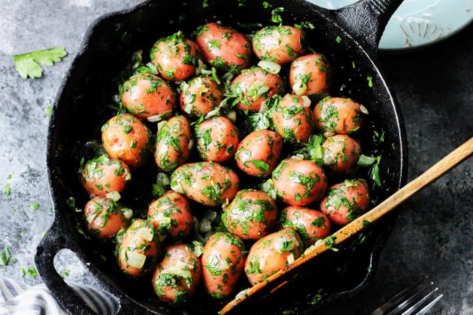 Overhead shot of parsley potatoes in a skillet with wooden spoon