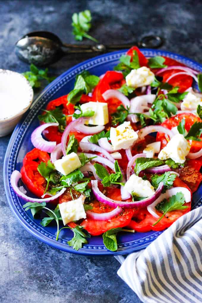Tomato Feta Salad on a blue serving plate with spoon at the back and kitchen towel