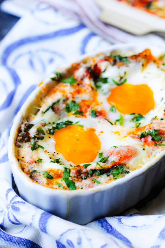 Oven baked eggs with tomato spinach cream sauce in a white baking dish with kitchen towel