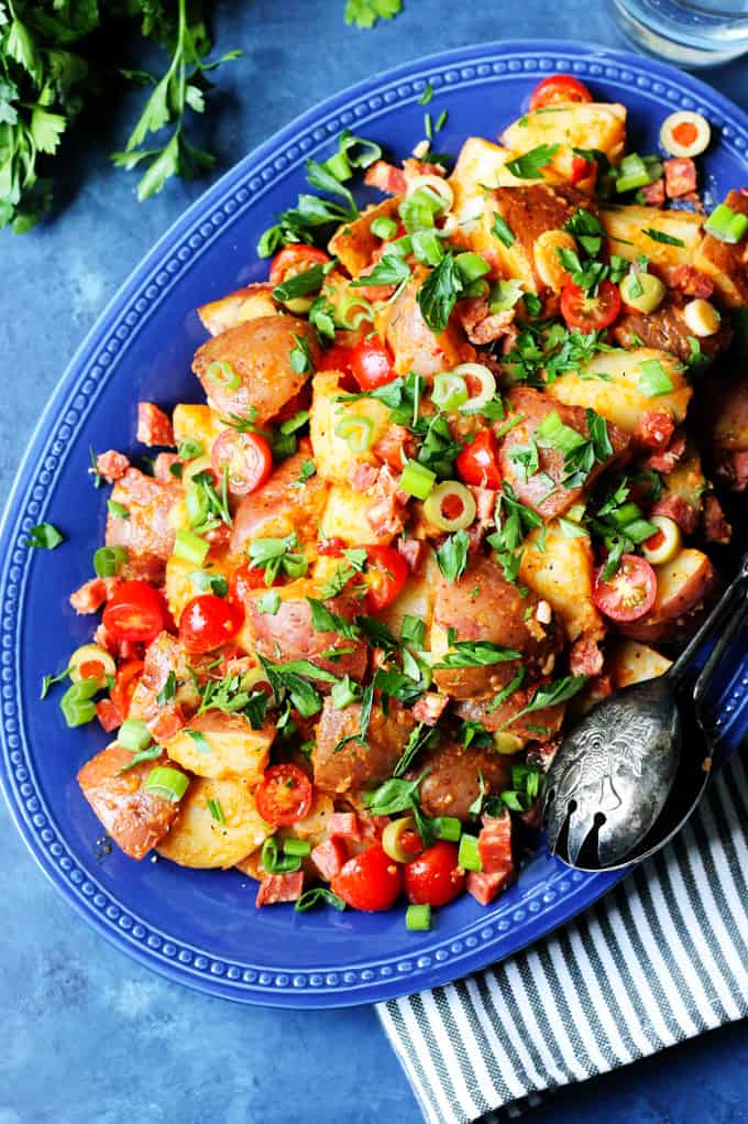 Smoky Spanish Potato Salad without mayo on a blue serving platter with serving spoon on a side