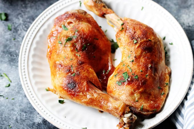 Horizontal photo of slow roasted chicken leg quarters on a white plate