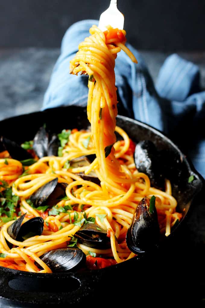 Fork picking up pasta from a skillet with bucatini and mussels