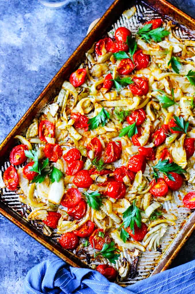 Roasted fennel and cherry tomatoes on a baking sheet with blue background