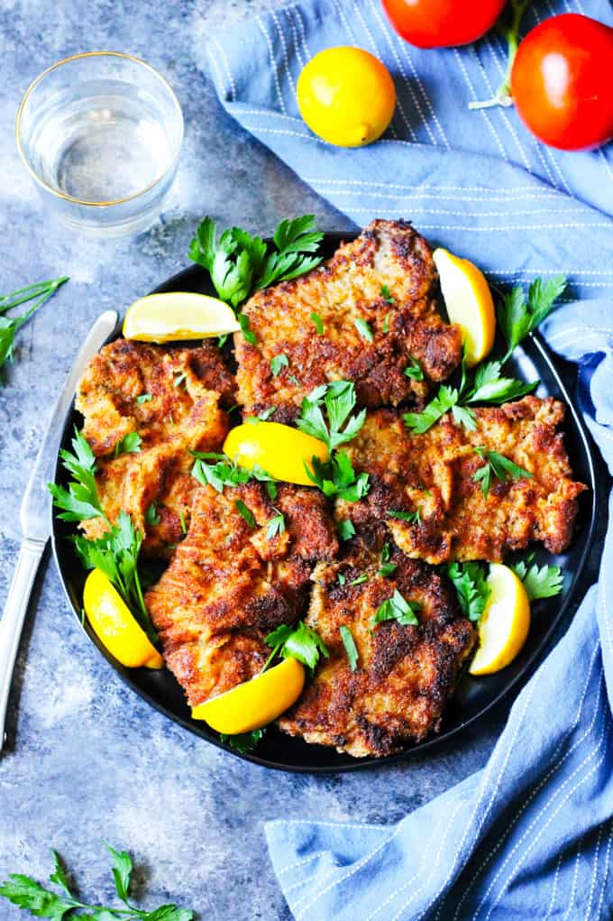 Veal cutlets Milanese style on a round black plate with blue background