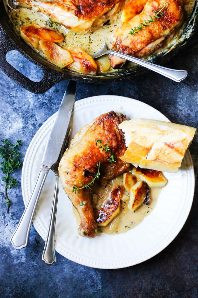 Chicken normandy on a white plate with skillet in the back