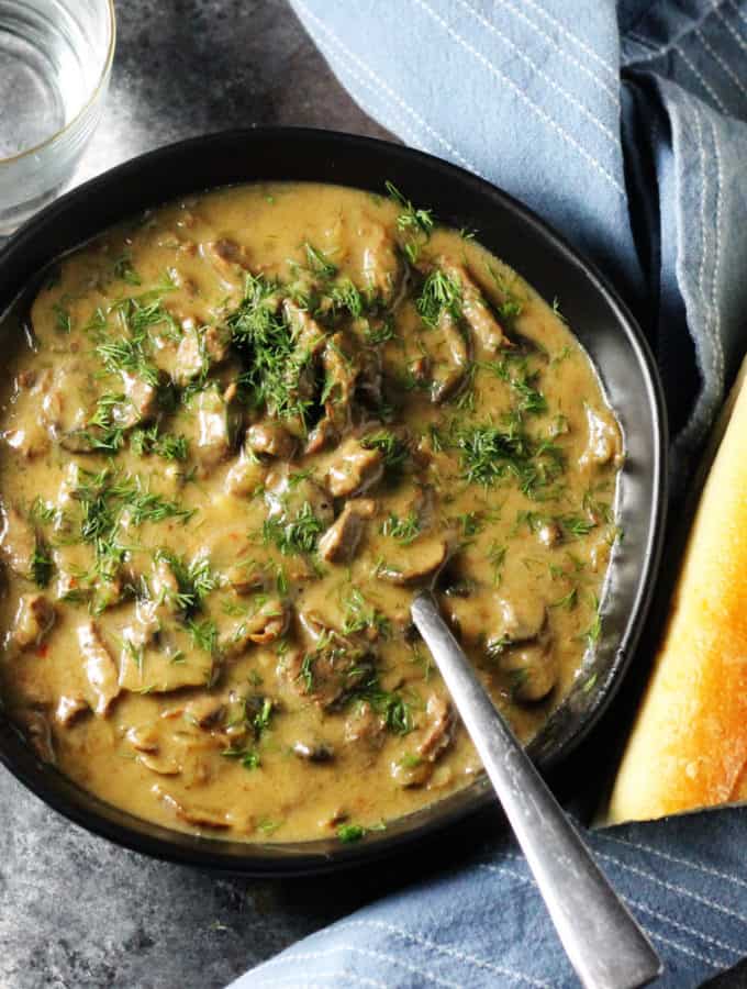 Beef Stroganoff in a black bowl with spoon and bread on a side