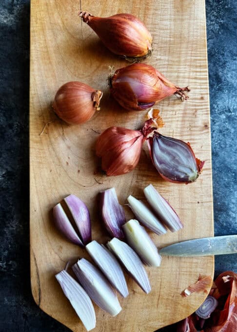 Shallots being cut up on a wooden cutting board