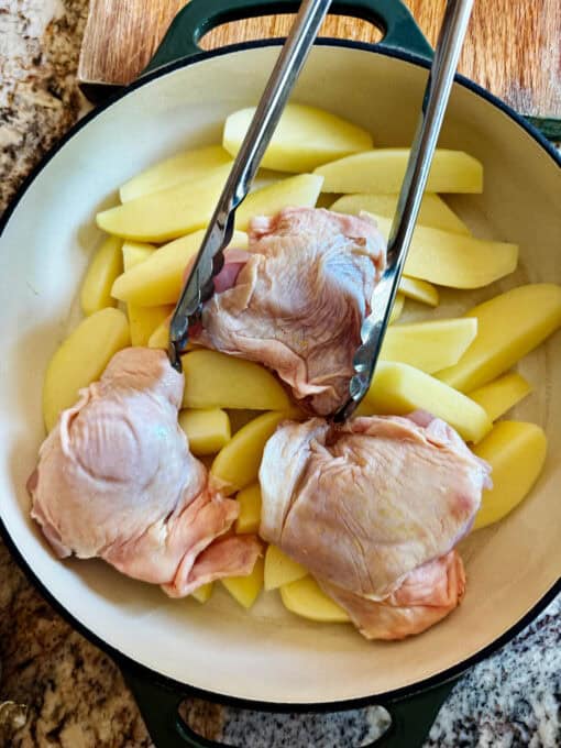 Chicken thighs being placed over the pottoes