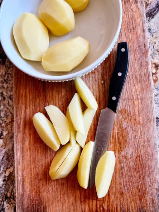 Potatoes cut into quarters on a chopping board